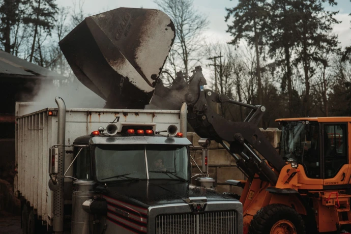 Industrial front-end loader filling a delivery truck with premium bulk garden soil at the farm.