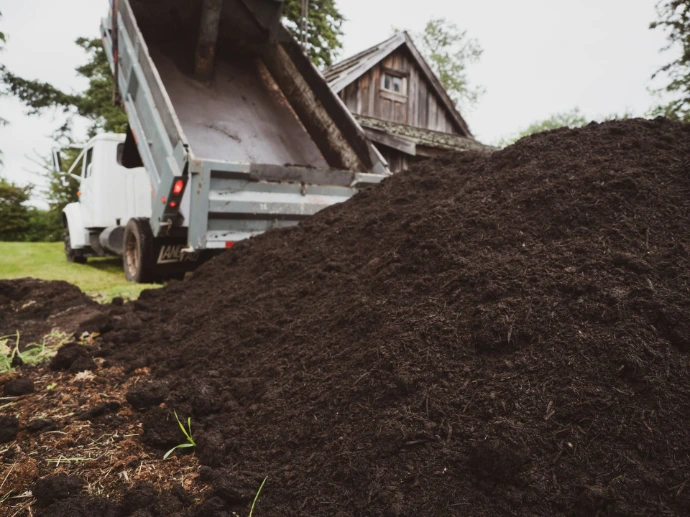 A large pile of dark, nutrient-rich organic topsoil freshly delivered to a residential driveway.