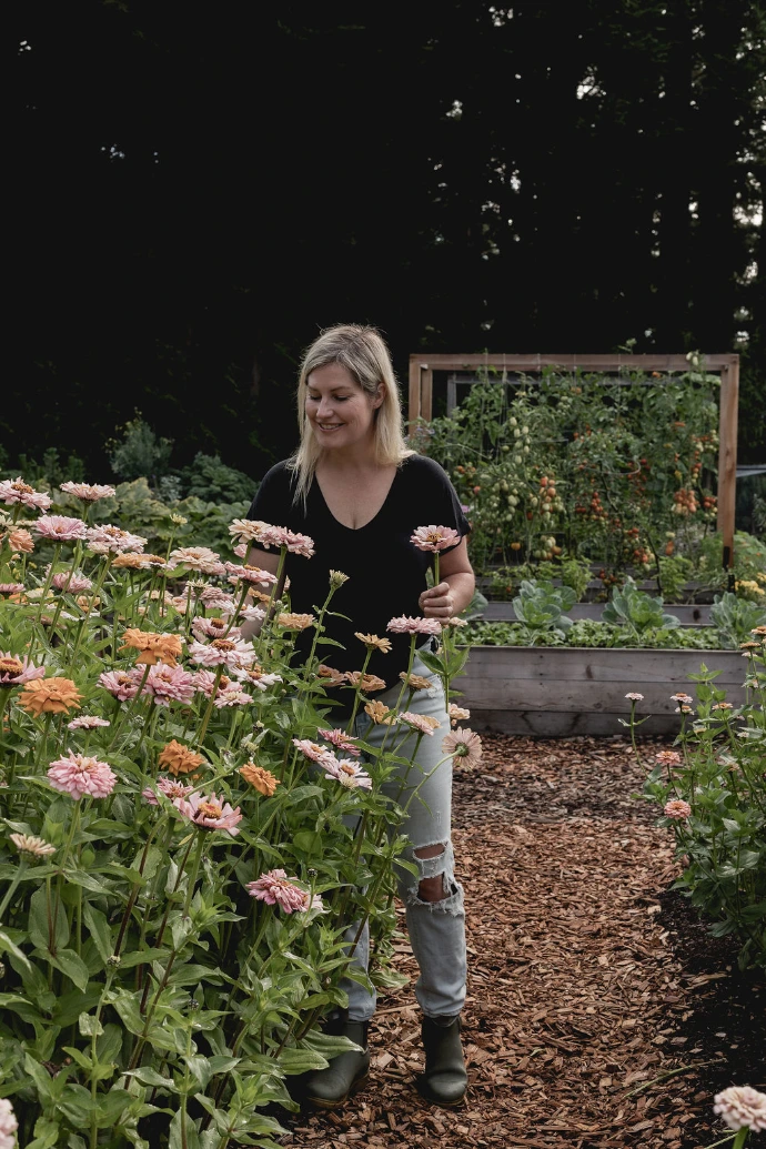A gardener standing among blooming pink and white flowers in a thriving farm-to-garden field.