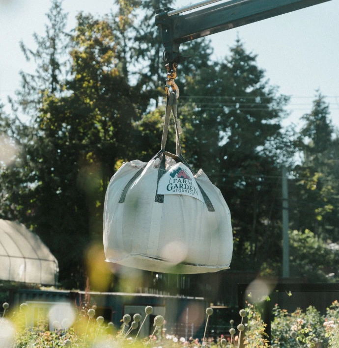 Crane delivery of a heavy-duty bulk bag filled with farm-developed soil for home gardening.